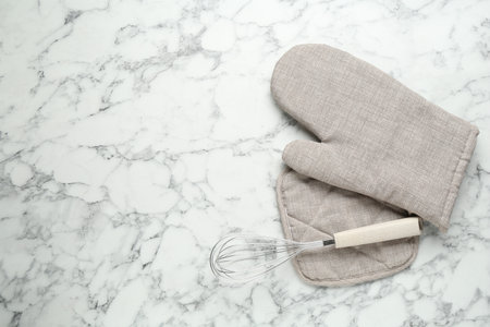 Oven glove, potholder and whisk on white marble table, flat lay. Space for textの写真素材