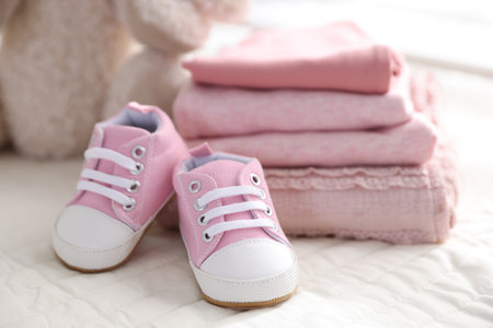 Stack of clean baby clothes and shoes on bed linens, closeupの写真素材