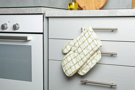 Oven glove and potholder hanging on handle of cabinet in kitchenの写真素材