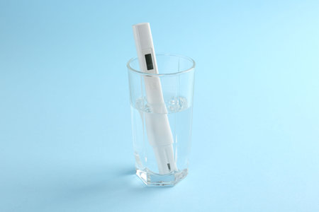 Nitrate tester in glass of water on light blue background