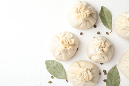 Uncooked khinkalis (dumplings) with peppercorns and bay leaves on white table, flat lay. Space for textの写真素材
