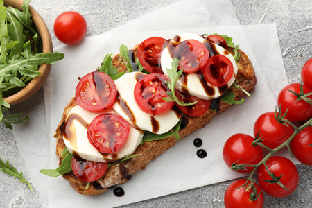 Delicious sandwich with mozzarella cheese, balsamic sauce, tomatoes and arugula on gray table, flat layの写真素材