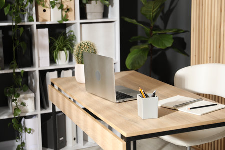 Stylish workplace with laptop, stationery and floral decor in office. Biophilic interior designの写真素材