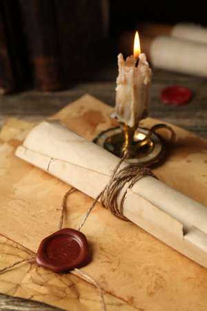 Old rolled paper scroll, sheets and burning candle on wooden table, closeupの写真素材