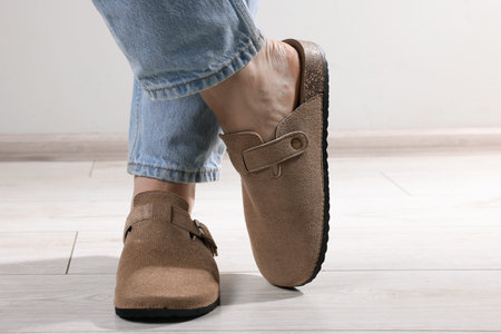 Woman in stylish beige slippers on light wooden floor, closeup