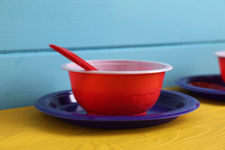 Set of disposable plastic tableware on yellow wooden table against light blue background, closeupの写真素材