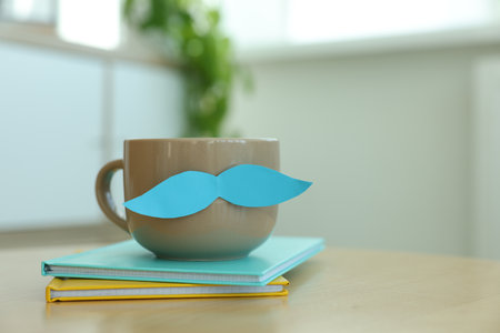 Happy Father's Day. Cup with mustache and notebooks on wooden table indoors, closeup. Space for textの写真素材