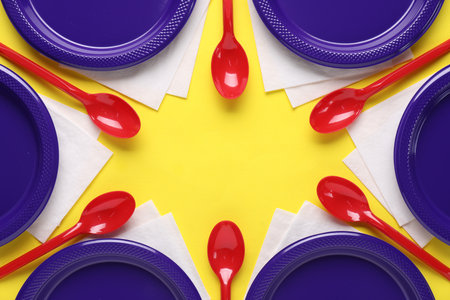 Frame of disposable plastic tableware and paper napkins on yellow background, flat lay. Space for textの写真素材