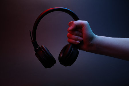 Woman holding wireless headphones on dark background, closeupの写真素材
