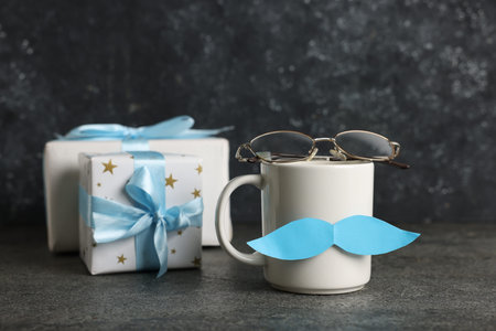 Happy Father's Day. Cup with paper mustache, gift boxes and glasses on black table, closeupの写真素材