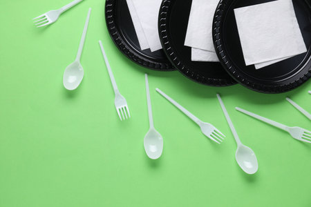 Set of disposable plastic tableware and paper napkins on green background, flat layの写真素材