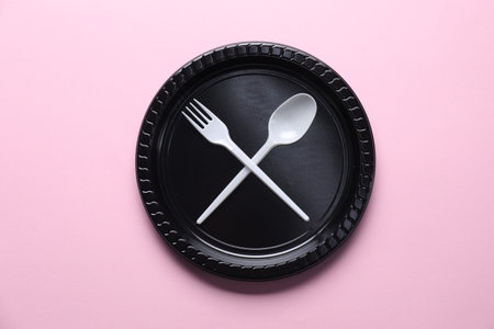 Disposable plastic plate and cutlery on pink background, top view
