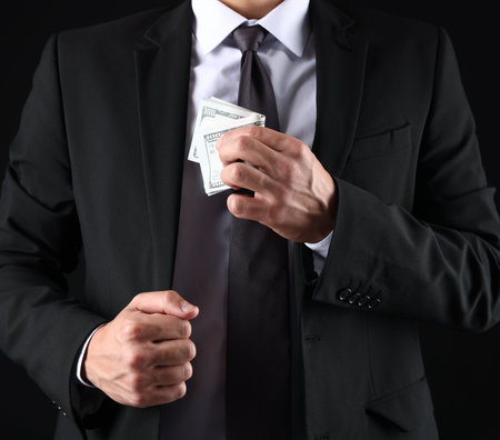 Man putting dollars in pocket on black background, closeupの写真素材