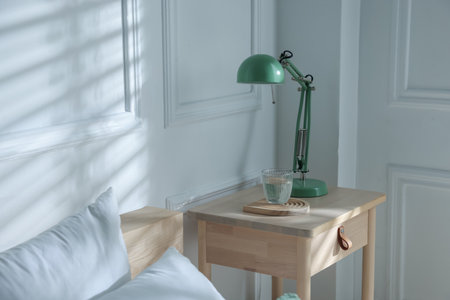 Bedside table with lamp and glass of water near bed indoorsの写真素材