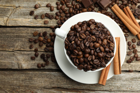 Aromatic coffee beans in cup, cinnamon and pieces of chocolate on wooden table, flat lay. Space for...