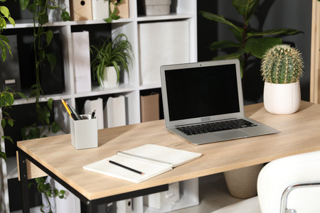 Stylish workplace with laptop, stationery and floral decor in office. Biophilic interior designの写真素材