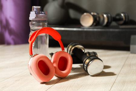 Wireless headphones, bottle of water and dumbbells on floor in gym