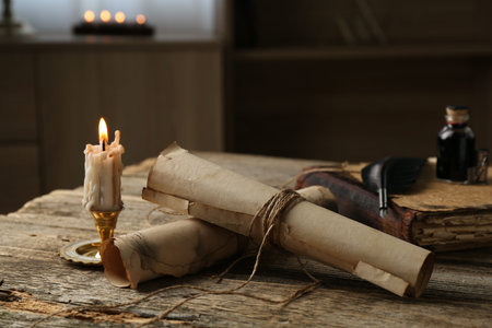 Old paper scrolls, book, feather, inkwell and burning candle on wooden table, closeup