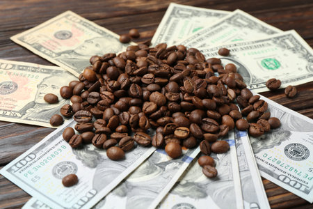 Pile of roasted coffee beans and dollar banknotes on wooden table, closeupの写真素材