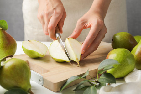 Woman cutting fresh ripe pear at white wooden table, closeupの写真素材