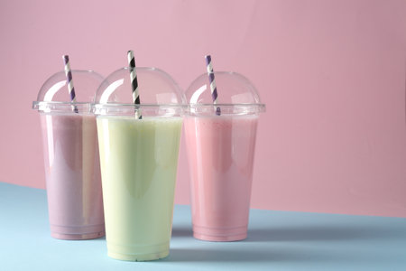 Tasty milkshakes in plastic cups on color background, space for textの写真素材