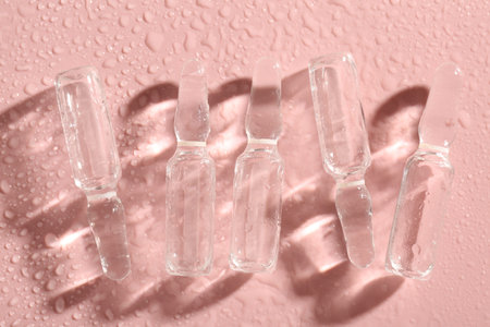 Glass ampoules with liquid and water drops on pink background, flat layの写真素材