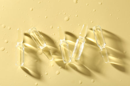 Glass ampoules with liquid and water drops on yellow background, flat layの写真素材