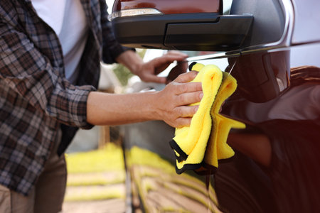 Man wiping car with yellow microfiber rag outdoors, closeupの写真素材