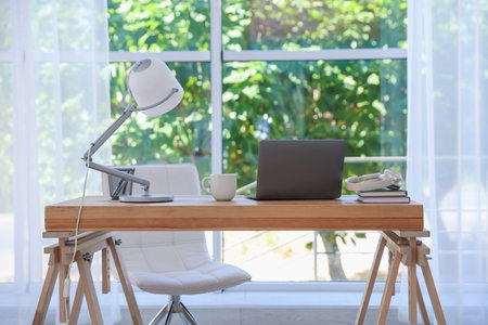 Home workspace. Laptop and stationery on wooden desk near window indoorsの写真素材