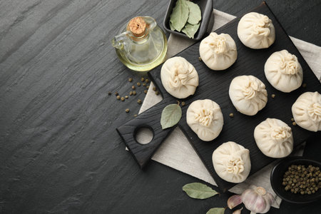 Uncooked khinkalis (dumplings) with peppercorns, garlic and bay leaves on black table, flat lay. Space for textの写真素材