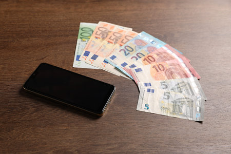 Smartphone and euro banknotes on wooden table, closeup