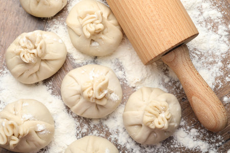 Uncooked khinkalis (dumplings) with rolling pin and flour on wooden table, flat layの写真素材