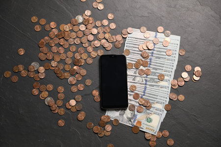 Smartphone, dollars and coins on black table, flat lay
