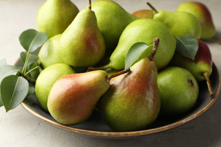 Fresh ripe pears and green leaves on light gray table, closeup