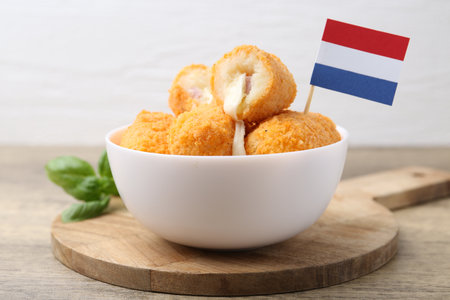 Delicious fried croquettes in bowl, flag of Netherlands and basil on wooden table, closeupの写真素材