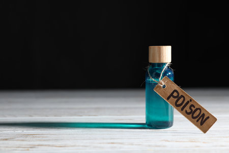 Bottle with poison on wooden table against black background, space for textの写真素材