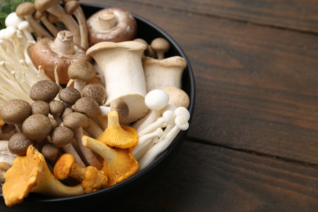 Different raw mushrooms in bowl on wooden table, closeup. Space for textの写真素材