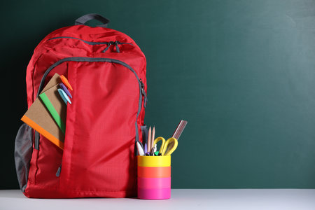 Red backpack with different stationery on table near blackboard. Space for textの写真素材