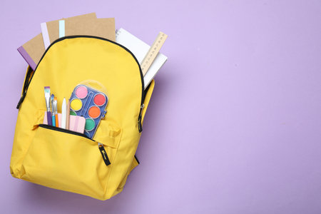 Yellow backpack with different stationery on violet background, top view. Space for textの写真素材