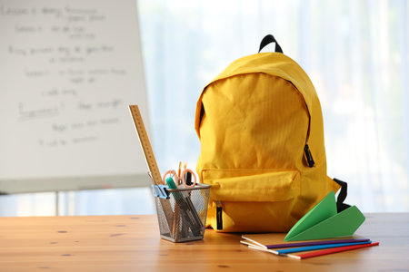 Backpack, different stationery and paper plane on desk in classroomの写真素材
