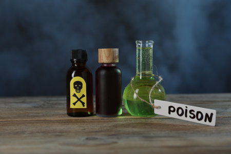 Bottles of poisons with warning sign on wooden table against dark background with smokeの写真素材