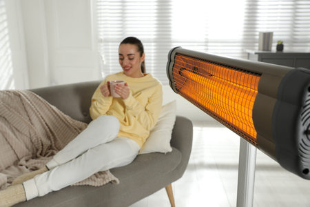 Woman on sofa in room with electric heater, selective focusの写真素材