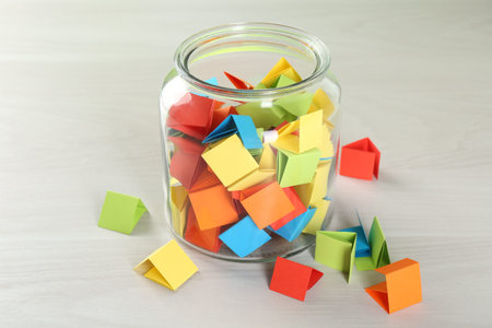 Colorful paper pieces in glass jar on wooden table, closeup