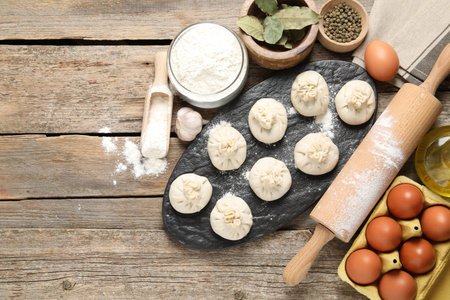 Uncooked khinkalis (dumplings), flour, spices, eggs and rolling pin on wooden table, flat lay. Space for textの写真素材
