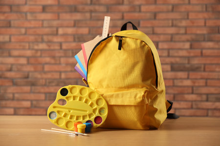 Yellow backpack with notebooks and art supplies on desk in classroomの写真素材