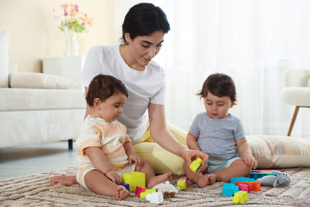 Mother with her cute little twins and toys on floor at home
