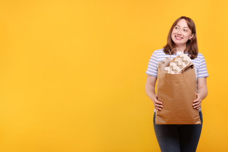 Recycling. Smiling woman with bag full of different waste paper on yellow background. Space for textの写真素材