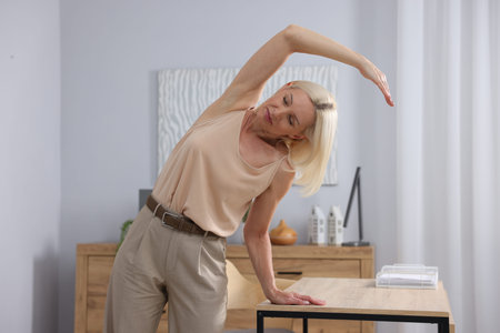 Mature woman stretching leaning on table in office