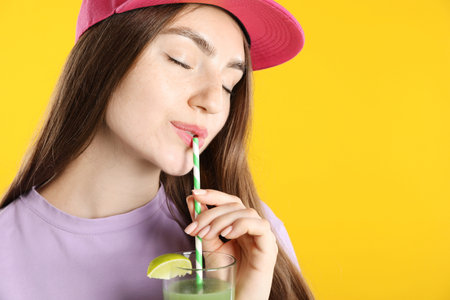 Woman drinking refreshing drink through straw on orange background, space for textの写真素材