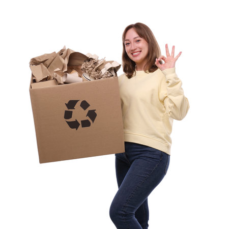Recycling. Smiling woman holding cardboard box with different paper waste and showing OK gesture on white backgroundの写真素材